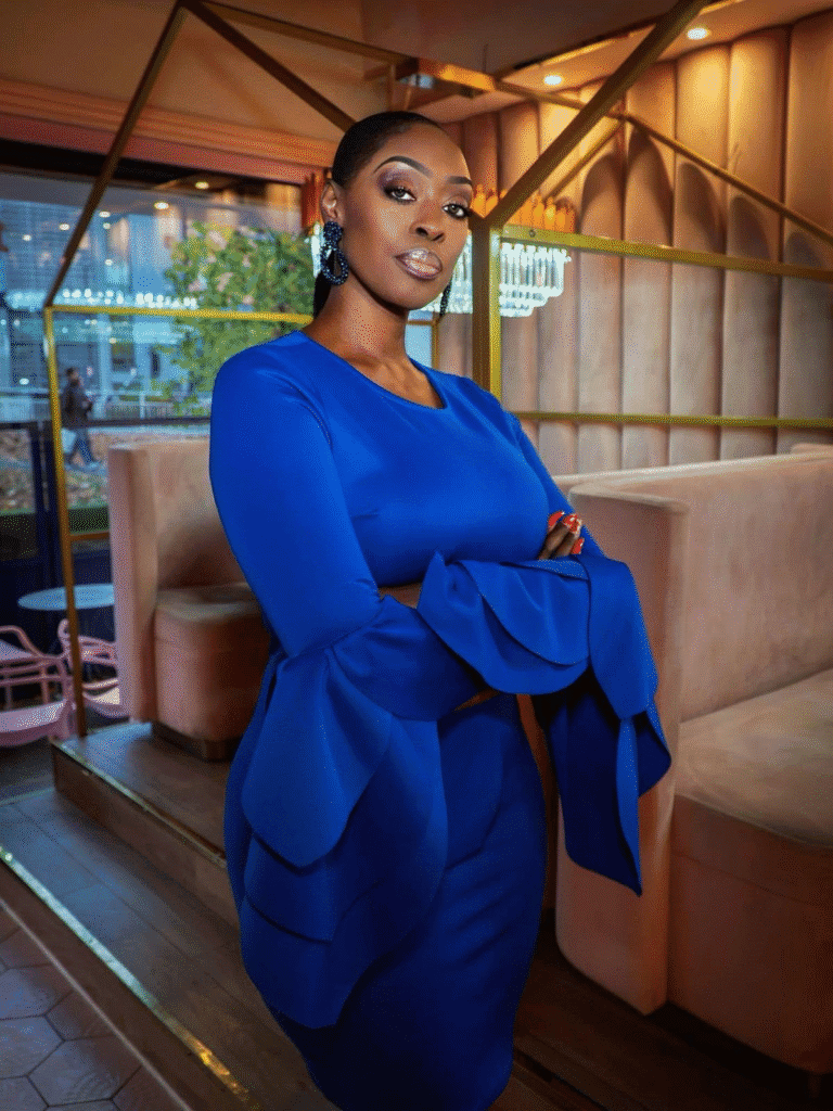 Dilys Sillah standing with folded arms in a blue dress inside a contemporary venue.